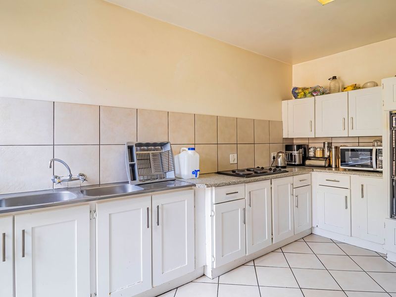 Functional kitchen featuring white cabinetry, tiled backsplash, double sink, built-in oven, and gas hob with tiled flooring throughout.