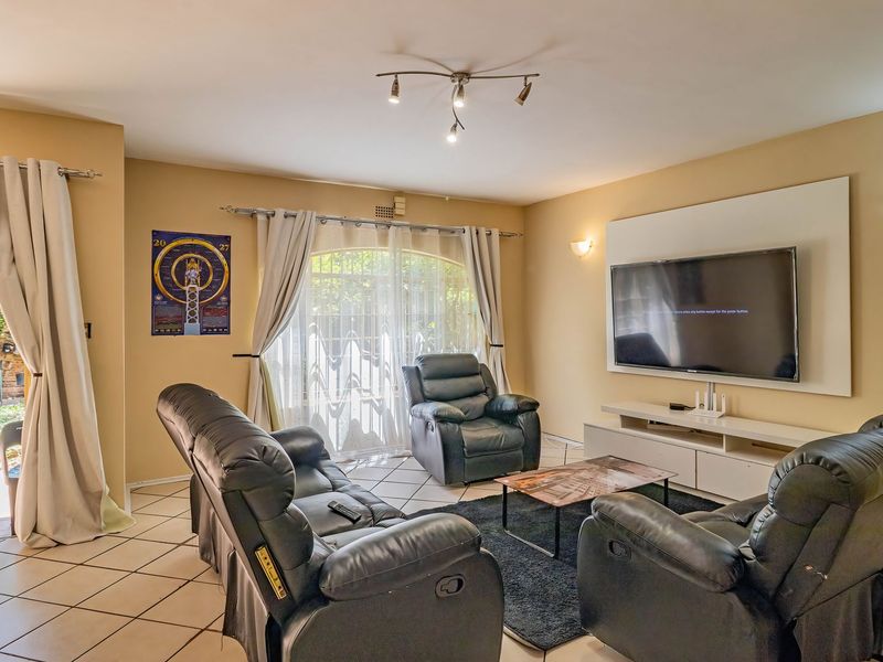A comfortable living room featuring tiled flooring, wall-mounted television panel, and direct access to the rear garden through a sliding glass door.