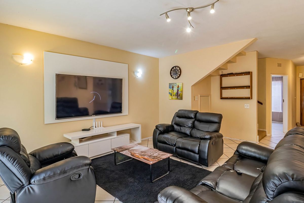 A spacious living room featuring tiled flooring, wall-mounted lighting, and a staircase leading to the upper level.