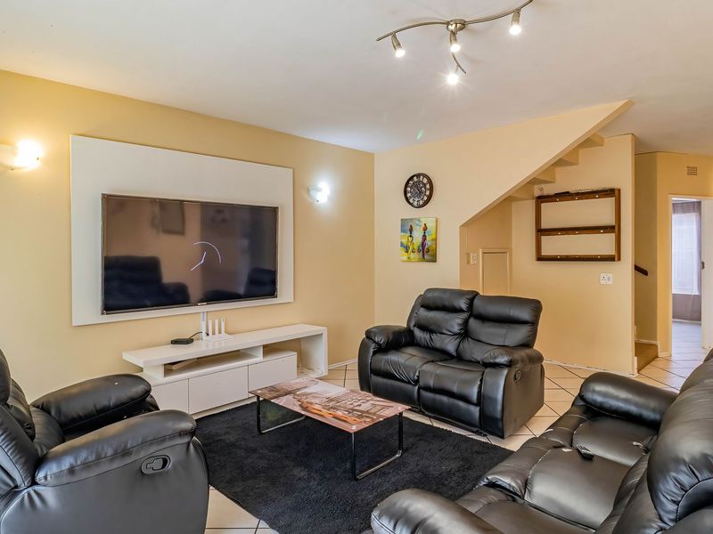 A spacious living room featuring tiled flooring, wall-mounted lighting, and a staircase leading to the upper level.