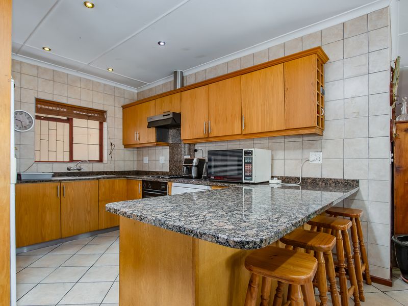 Functional kitchen featuring granite countertops, wooden cabinetry, a breakfast bar, and a tiled backsplash, providing a practical workspace for daily cooking.