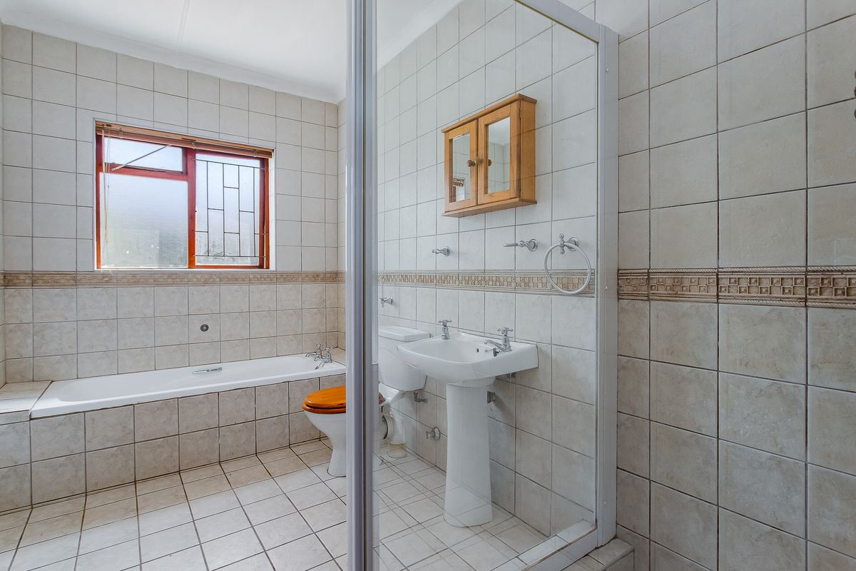 A functional bathroom featuring a built-in bathtub, pedestal sink, toilet, and a separate shower enclosure with full-height wall tiling.