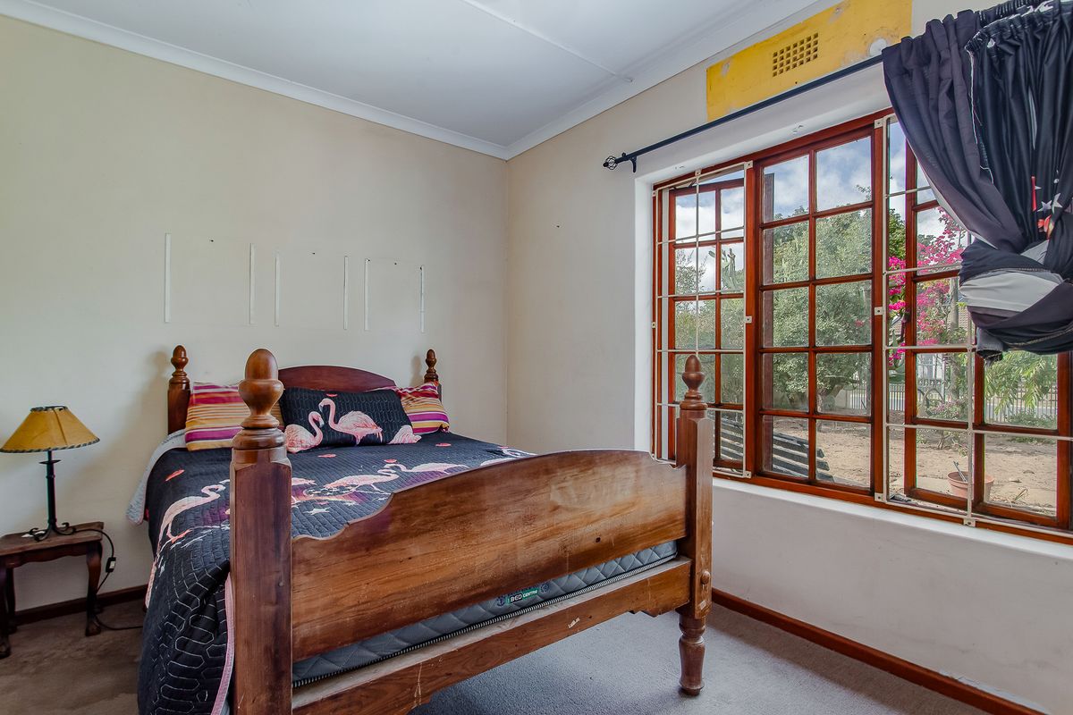 A bedroom featuring timber-framed windows and carpeted flooring, requiring minor cosmetic updates to the wall finishes and ventilation fixtures.