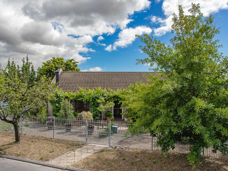 Front view of a single-story house featuring a tiled roof, a covered patio area, and a metal perimeter fence with a paved walkway.
