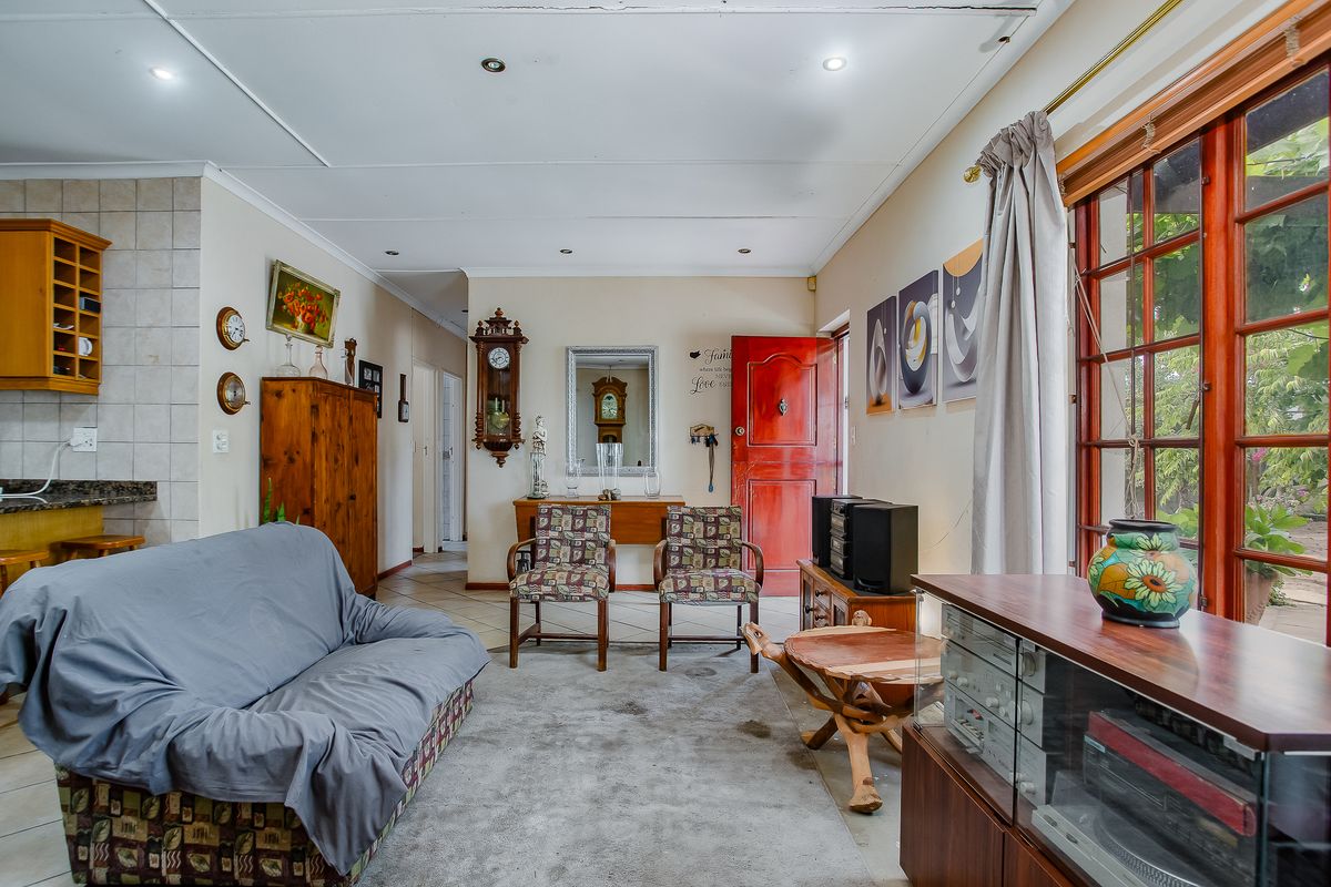 A living room featuring tiled flooring, recessed ceiling lighting, and timber-framed windows providing natural light and access to the exterior.
