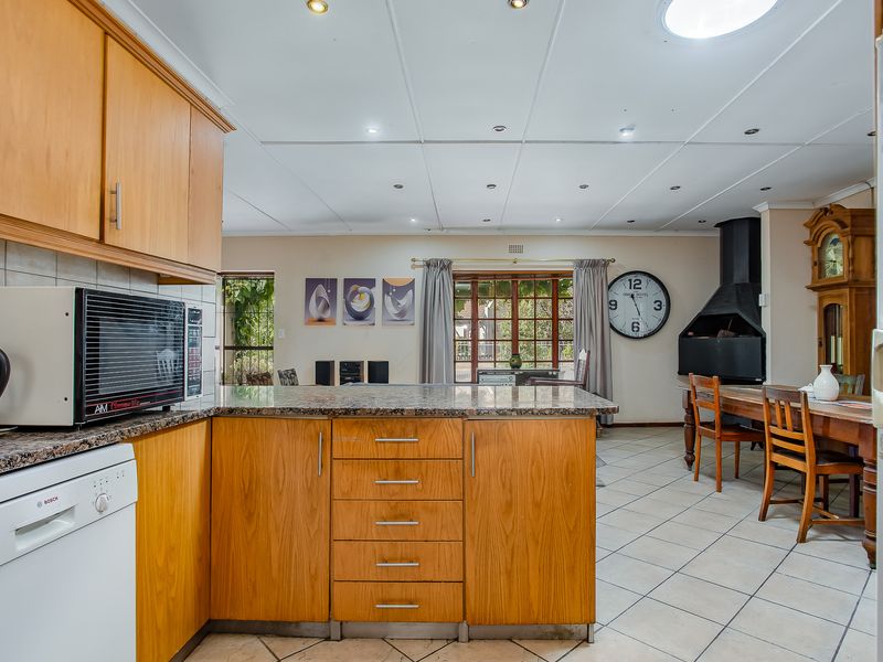 Open-plan kitchen and dining area featuring wooden cabinetry, granite countertops, tiled flooring, and a built-in fireplace, offering a functional and connected living space.