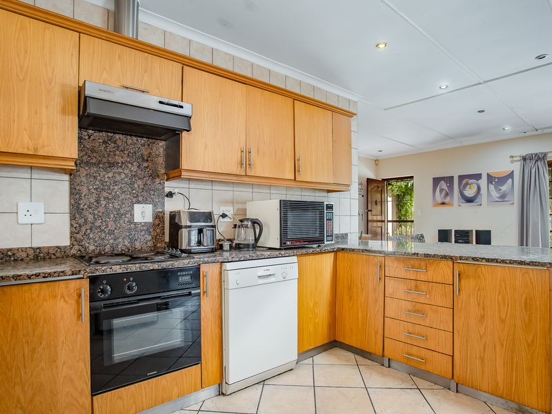 A functional kitchen featuring wooden cabinetry, granite countertops, built-in oven, electric hob, and tiled flooring, offering a practical layout for daily use.