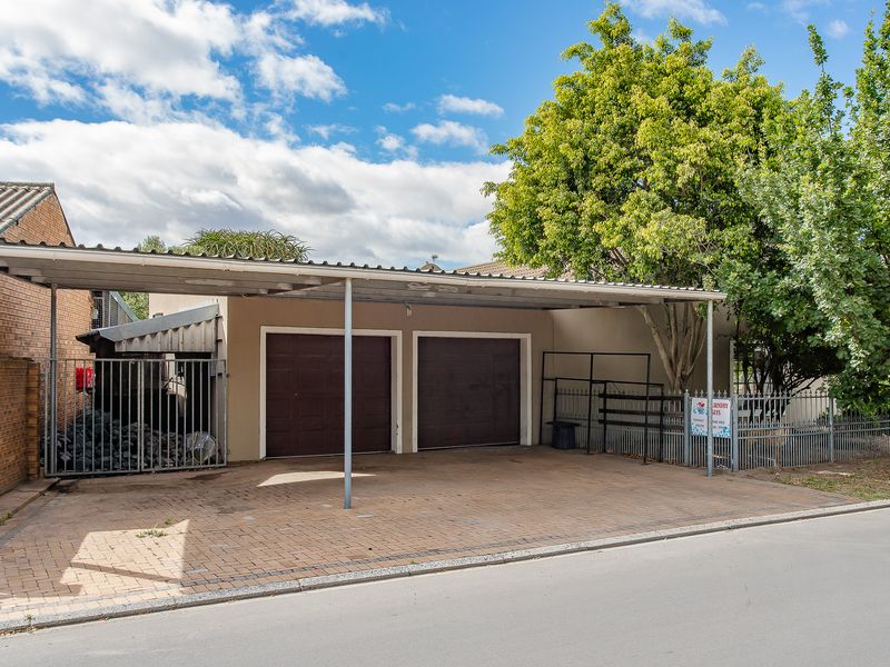 Front view of the property featuring a double garage with a covered carport and paved driveway, secured by metal fencing and a gate.
