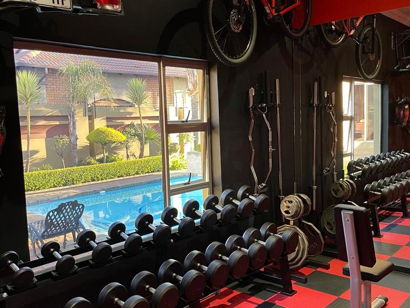 A well-equipped home gym featuring rubberized flooring, mirrored walls, and large windows overlooking the swimming pool area.