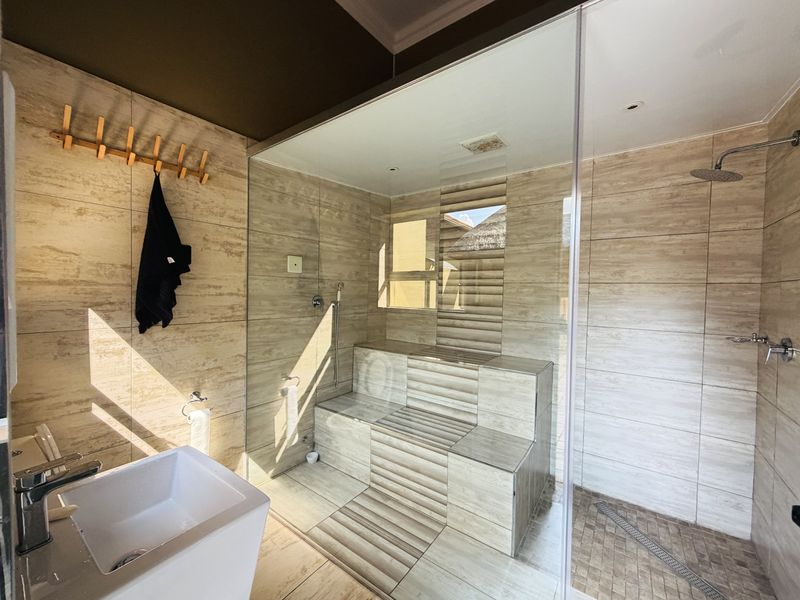 Modern bathroom featuring a spacious walk-in shower with a glass enclosure, built-in tiled bench, rain shower head, and contemporary wall-mounted basin.