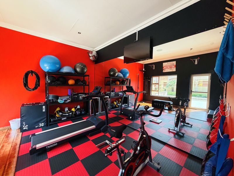 A dedicated home gym featuring high-contrast red and black walls, durable rubberized flooring, and direct access to the exterior through a glass door.