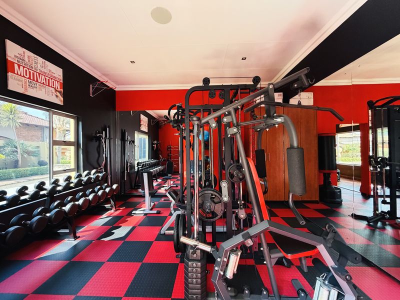 A dedicated home gym featuring rubberized flooring, recessed lighting, and a large mirrored wall, providing a functional space for fitness and training.