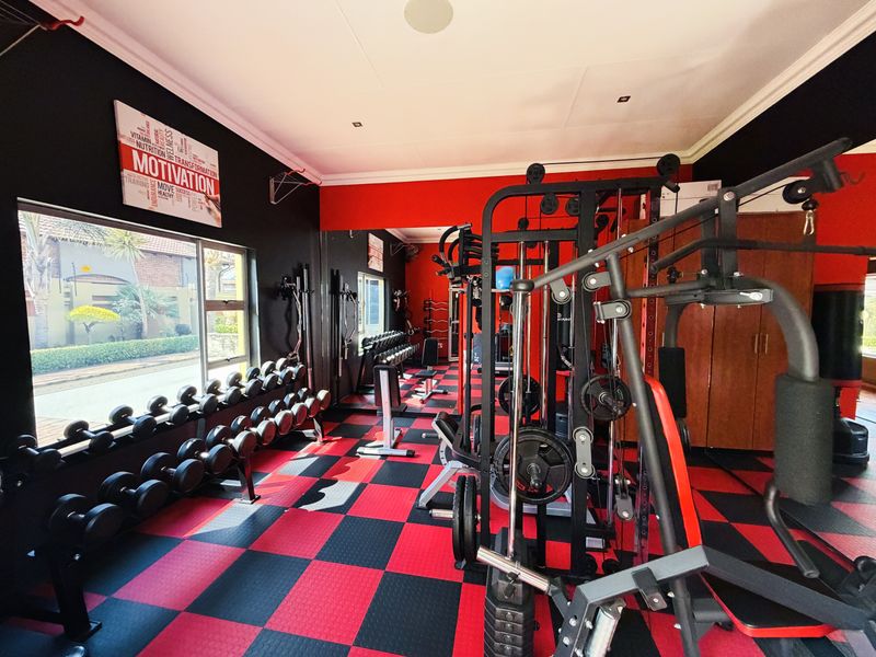 A dedicated home gym featuring rubberized flooring, recessed lighting, and ample space for strength training equipment with natural light from a large window.