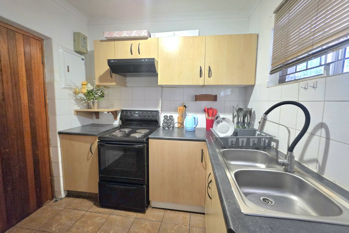 A functional kitchen featuring laminate cabinetry, a double bowl stainless steel sink, and an electric stove with an extractor fan.