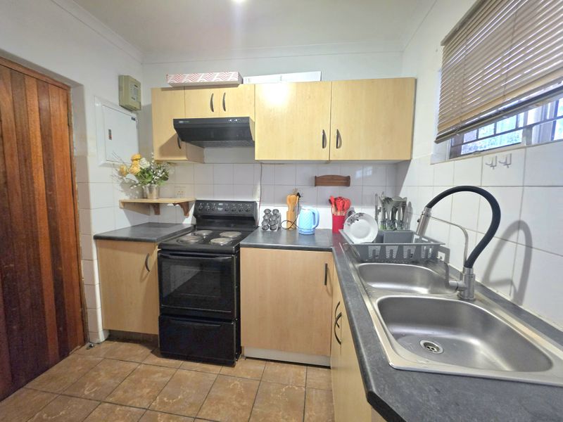 A functional kitchen featuring laminate cabinetry, a double bowl stainless steel sink, and an electric stove with an extractor fan.