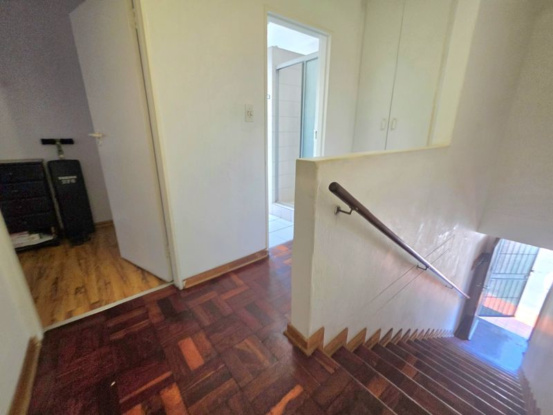 A hallway area featuring parquet flooring, a staircase with a handrail, and built-in storage cupboards, leading towards an adjacent room.