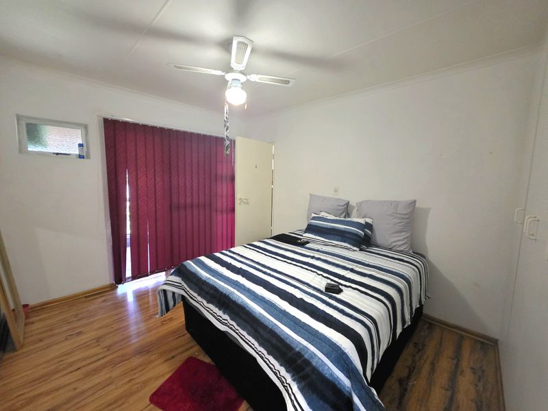 A functional bedroom featuring laminate flooring, a ceiling fan, and built-in storage cupboards, offering a neutral base for potential interior updates.