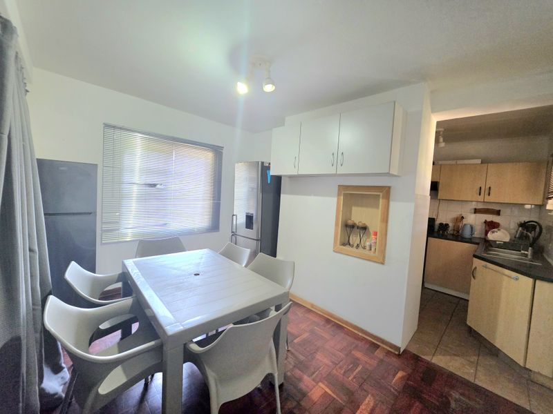 Open plan dining area featuring parquet flooring and venetian blinds, leading into a functional kitchen with built-in cabinetry and laminate countertops.