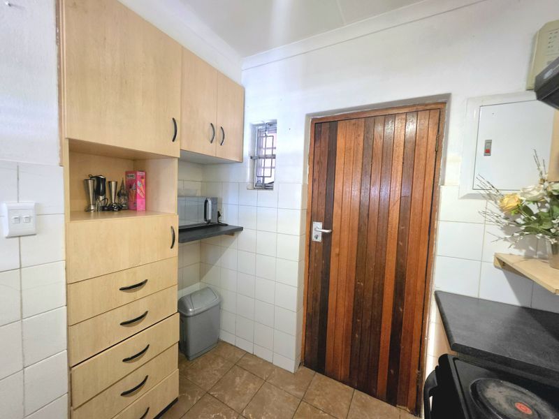 A functional kitchen area featuring built-in wooden cabinetry, tiled splashbacks, and a solid timber door, providing practical storage and workspace.