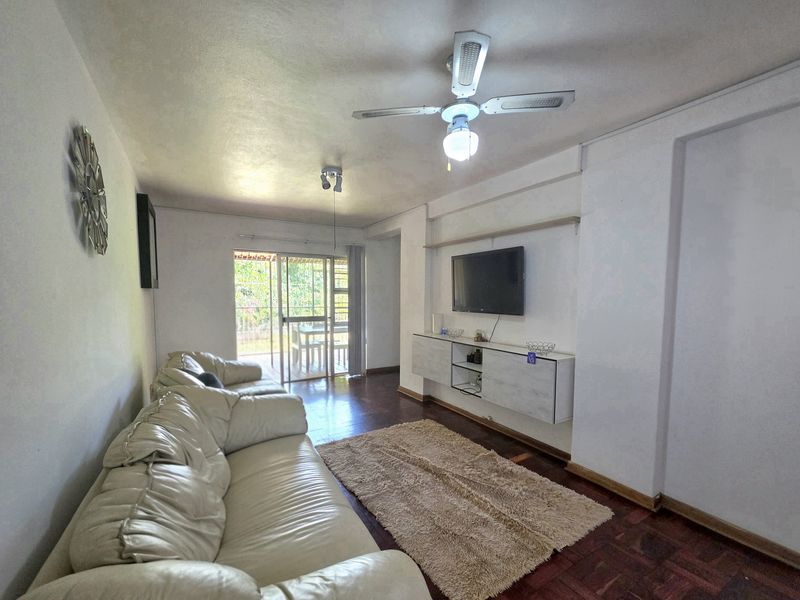 Spacious living room featuring parquet flooring, a ceiling fan, and a built-in media console, with direct access to an outdoor patio area.