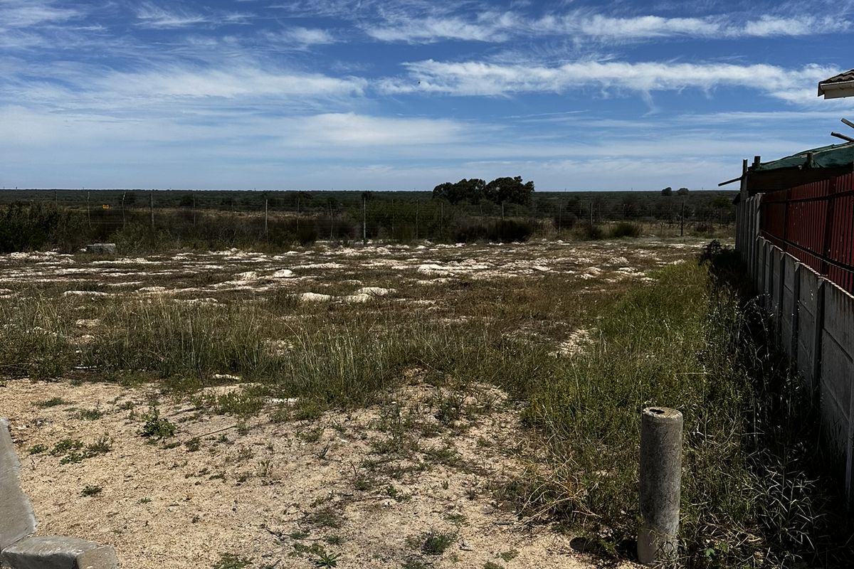 A vacant residential plot featuring a perimeter fence, concrete boundary wall, and natural ground cover, offering a clear view of the surrounding landscape.