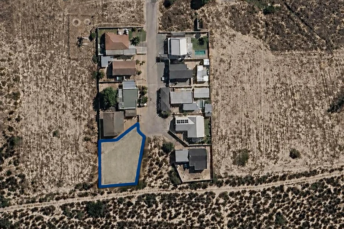Aerial view of a vacant residential land plot situated in a developed neighborhood, highlighting the property boundaries and surrounding landscape.