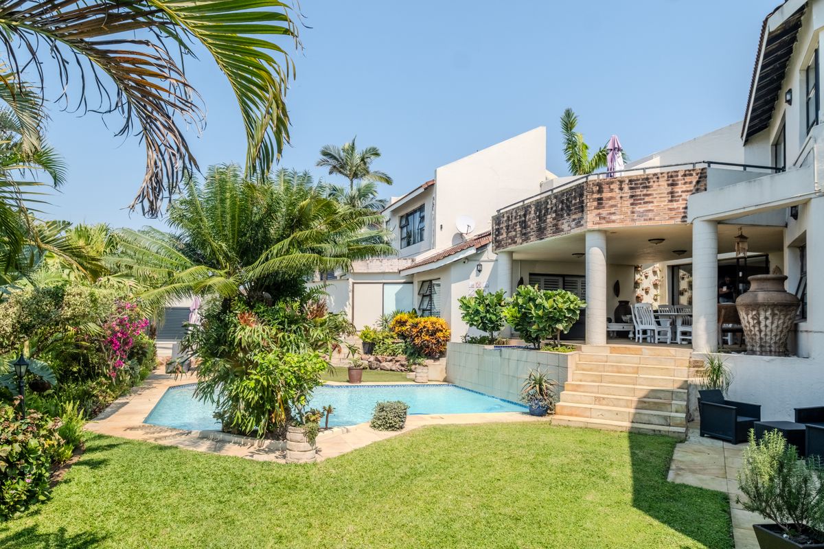 Rear view of the property featuring a swimming pool, landscaped garden, and a covered patio area with stone stairs leading to the main house.