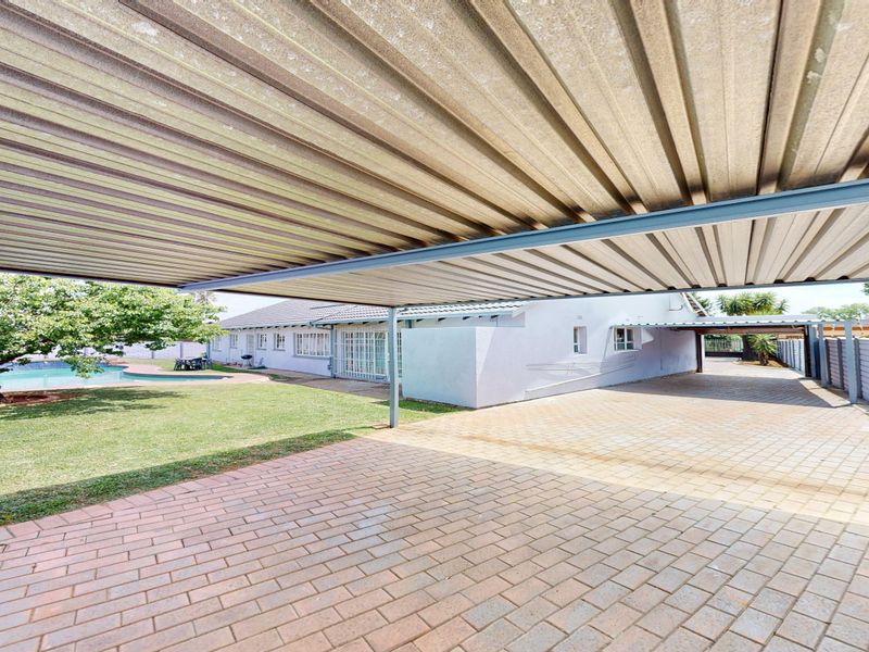 Rear exterior view featuring a paved driveway, a large corrugated metal carport, a swimming pool, and a well-maintained lawn area.