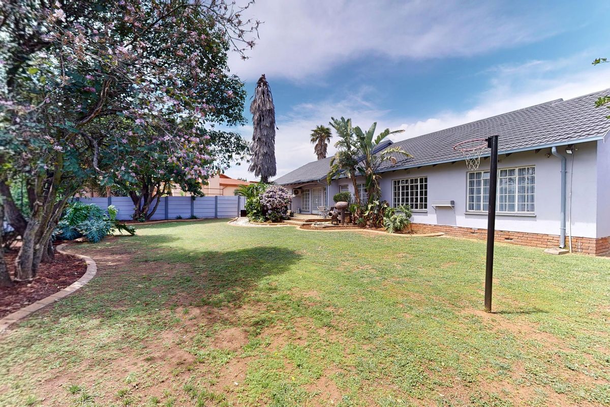 A spacious rear garden featuring a well-maintained lawn, established trees, and a brick perimeter wall, providing a private outdoor space for the home.