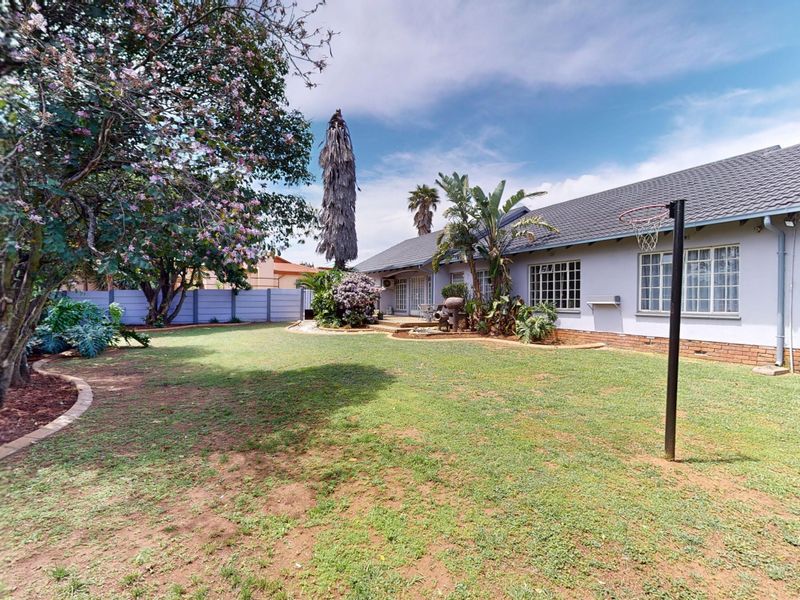A spacious rear garden featuring a well-maintained lawn, established trees, and a brick perimeter wall, providing a private outdoor space for the home.