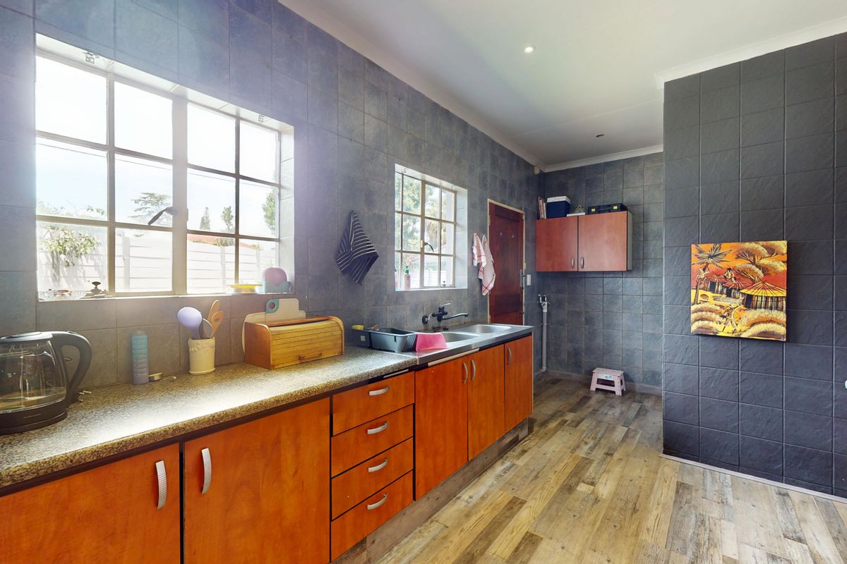 A functional kitchen featuring wood-toned cabinetry, laminate countertops, a stainless steel sink, and dark tiled wall finishes with wood-look flooring.