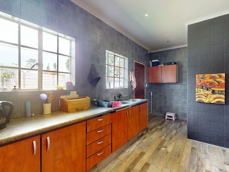A functional kitchen featuring wood-toned cabinetry, laminate countertops, a stainless steel sink, and dark tiled wall finishes with wood-look flooring.