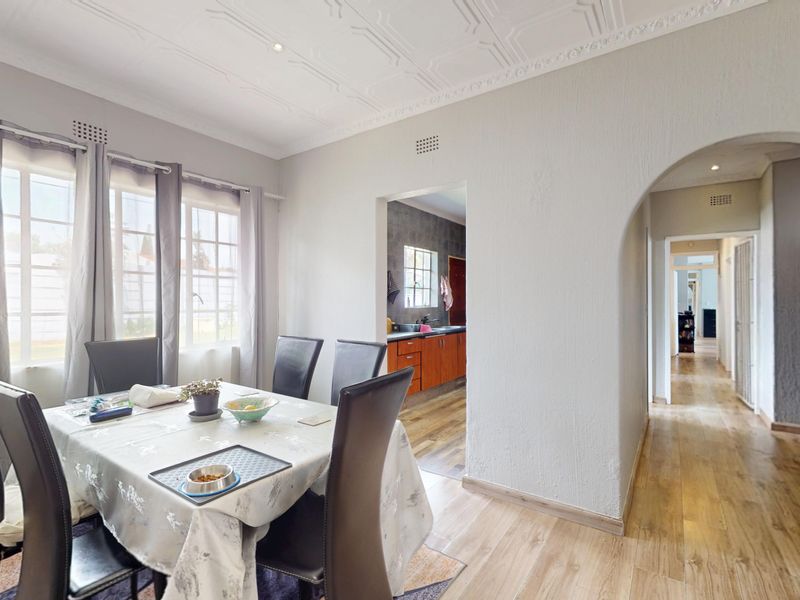 Bright dining room featuring decorative ceiling molding, laminate flooring, and an elegant archway leading to the kitchen and hallway.