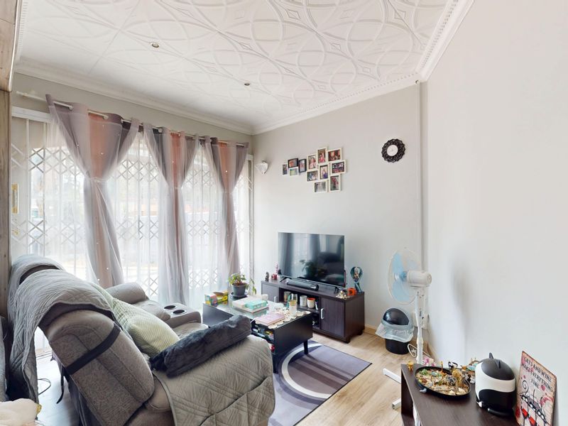 A comfortable living room featuring a decorative ceiling, laminate flooring, and a sliding door with security gate access to the exterior.
