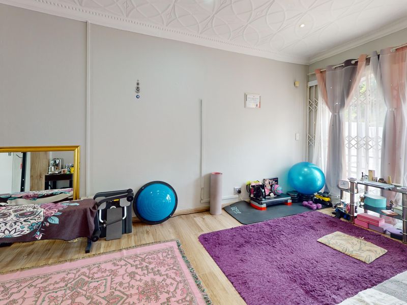 A bright living area featuring laminate flooring, decorative ceiling molding, and a sliding glass door with security gate access to the exterior.