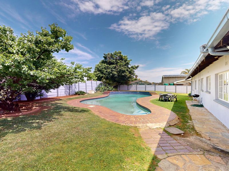 Rear garden featuring a swimming pool with brick coping, stone paved pathways, and a precast concrete boundary wall.