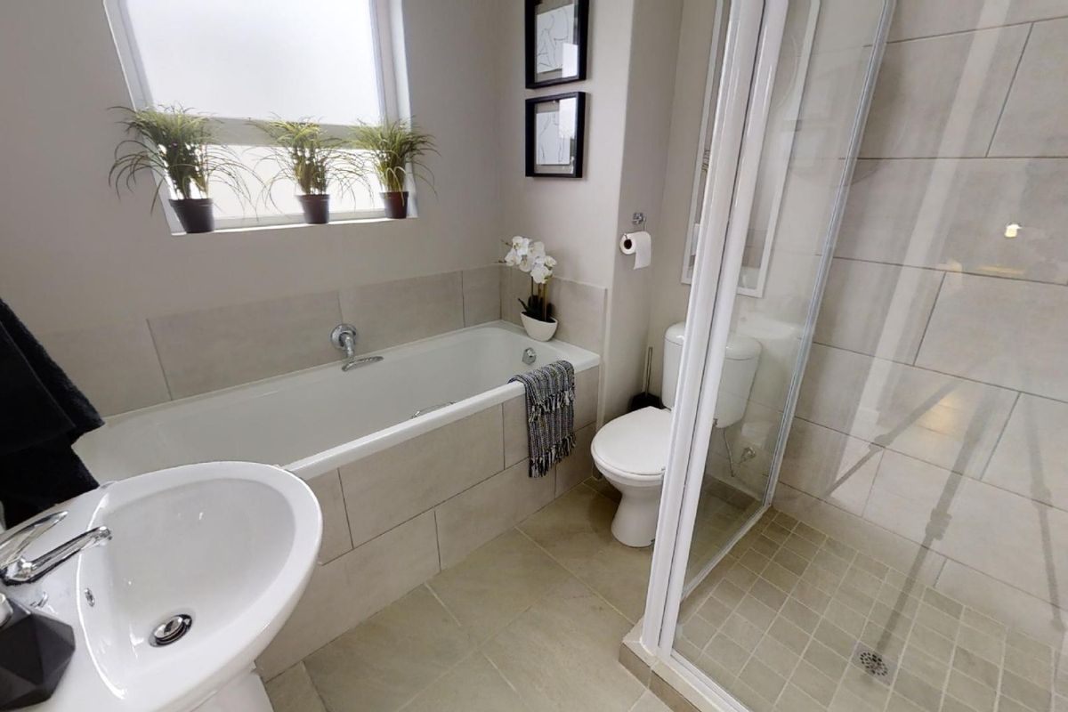 A modern, well-maintained bathroom featuring a built-in bathtub, a separate glass-enclosed shower, a pedestal basin, and neutral floor-to-ceiling tiling.