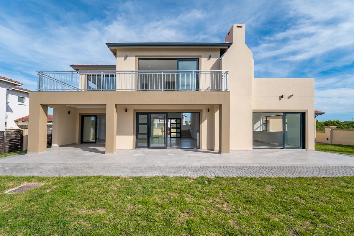 Rear view of a modern double-story house featuring a spacious covered patio, upper-level balcony with metal railing, and large sliding glass doors.
