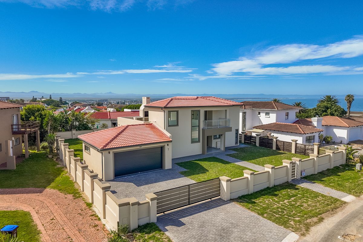 Aerial view of a modern double-story residential property featuring a tiled roof, paved driveway, double garage, and a secure boundary wall with a sliding gate.
