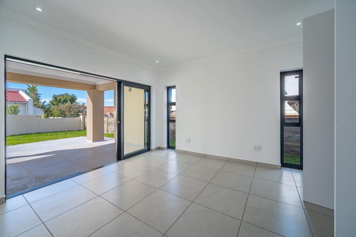 Bright and spacious living area featuring large sliding glass doors that open onto a covered patio and garden, with modern tiled flooring throughout.