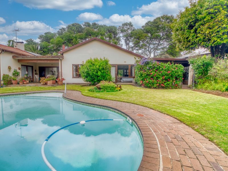 A well-maintained backyard featuring a swimming pool with brick paving, a lush lawn, and a covered patio area attached to the main house.