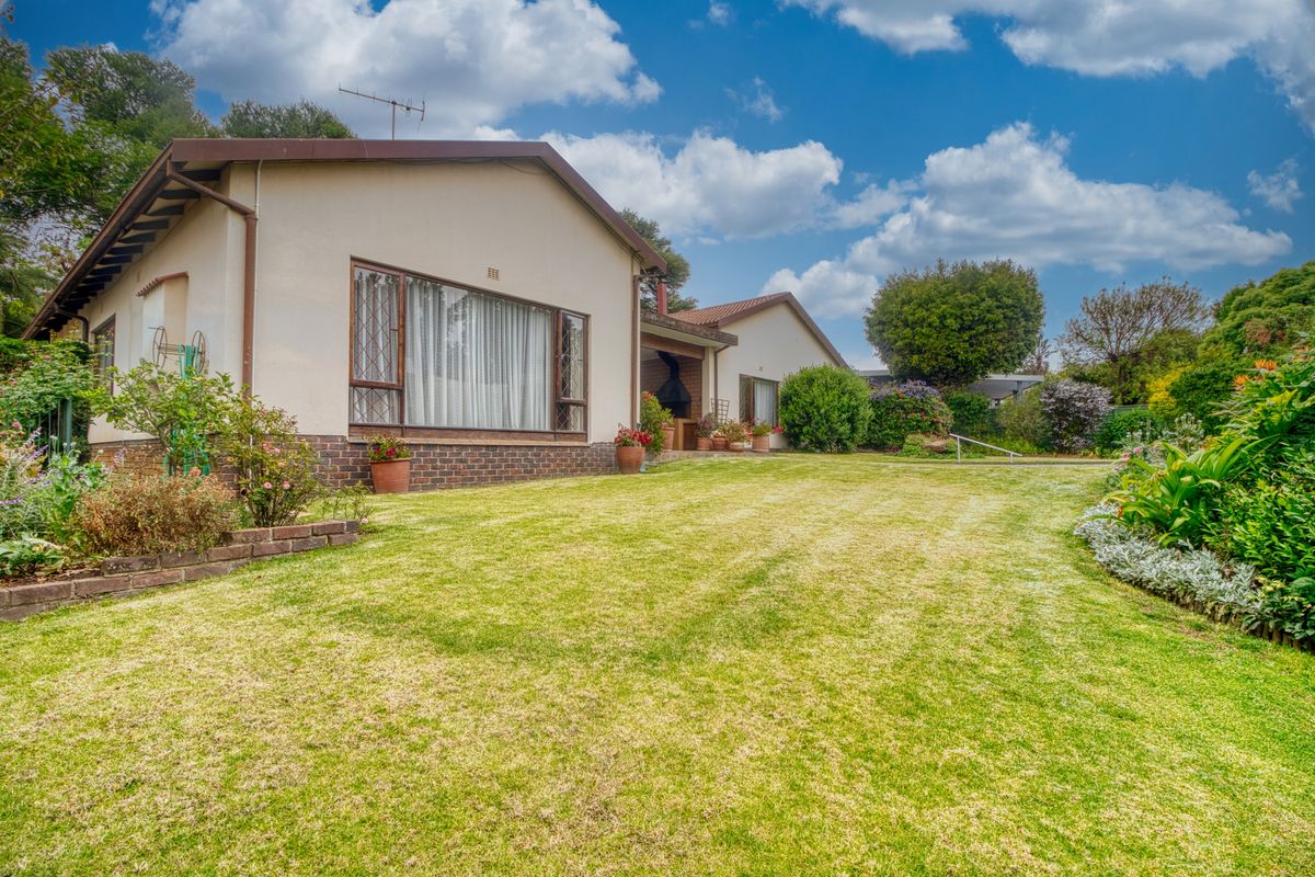 A well-maintained rear exterior view of the house featuring a spacious lawn, landscaped garden, and a built-in braai area.