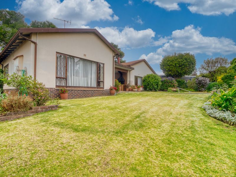 A well-maintained rear exterior view of the house featuring a spacious lawn, landscaped garden, and a built-in braai area.