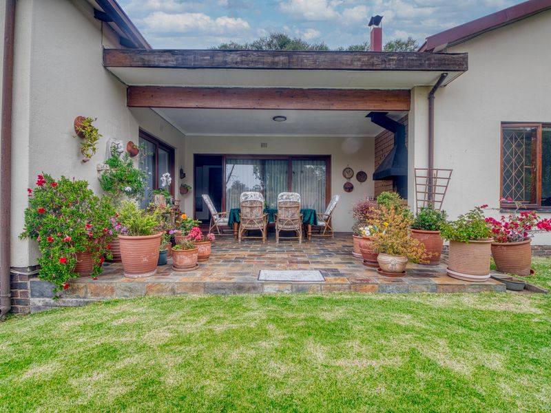 Covered outdoor patio featuring stone tile flooring, a built-in fireplace, and exposed timber beam detailing, overlooking the rear garden.