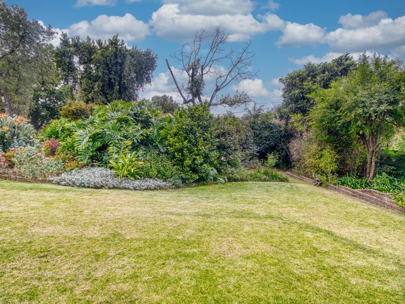 A well-maintained, lush garden featuring a manicured lawn and established mature plantings with brick edging.