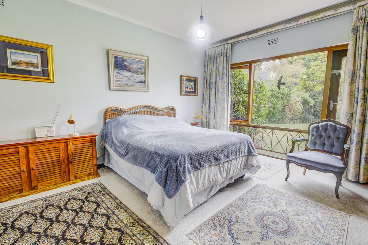 A well-lit bedroom featuring large windows with garden views, carpeted flooring, and neutral wall finishes, offering a comfortable and bright living space.