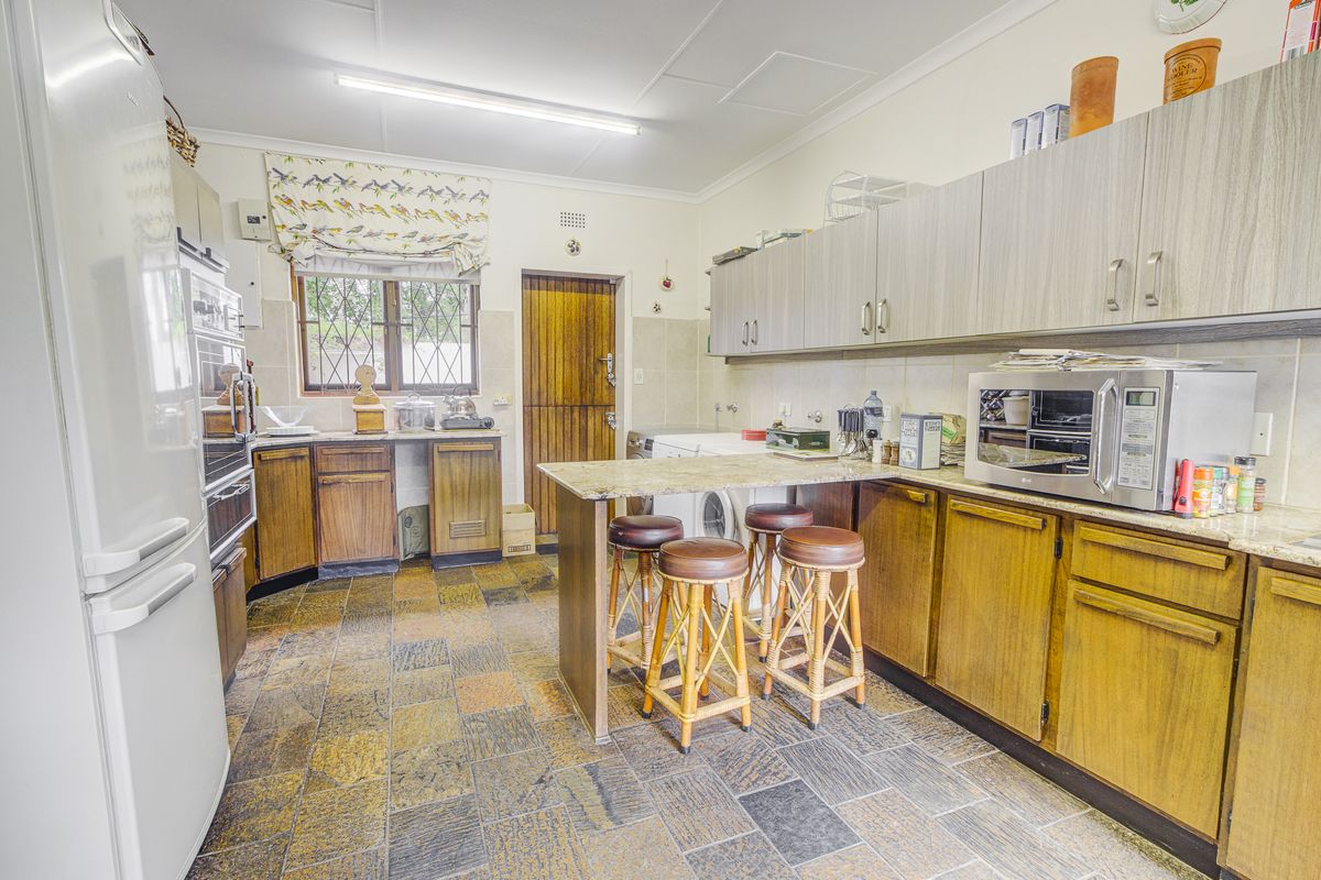 A functional kitchen featuring wood-toned cabinetry, stone countertops, built-in appliances, and durable stone tile flooring with a breakfast bar area.