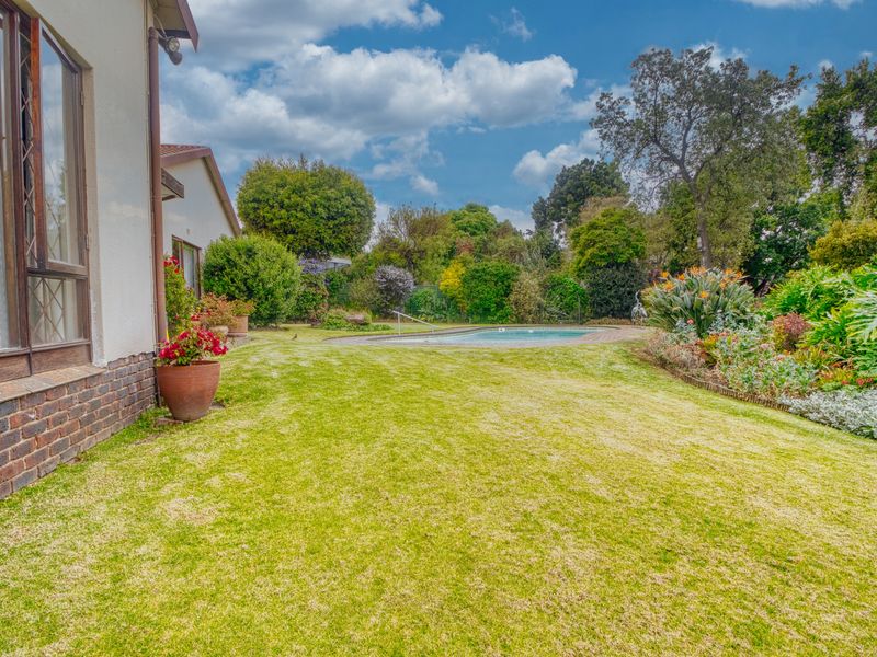 A spacious rear garden featuring a well-maintained lawn, established landscaping, and a swimming pool set against the rear elevation of the house.