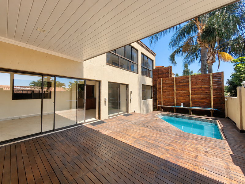 Spacious covered patio featuring wooden decking, direct access to the interior through sliding glass doors, and a private swimming pool with wooden privacy screening.