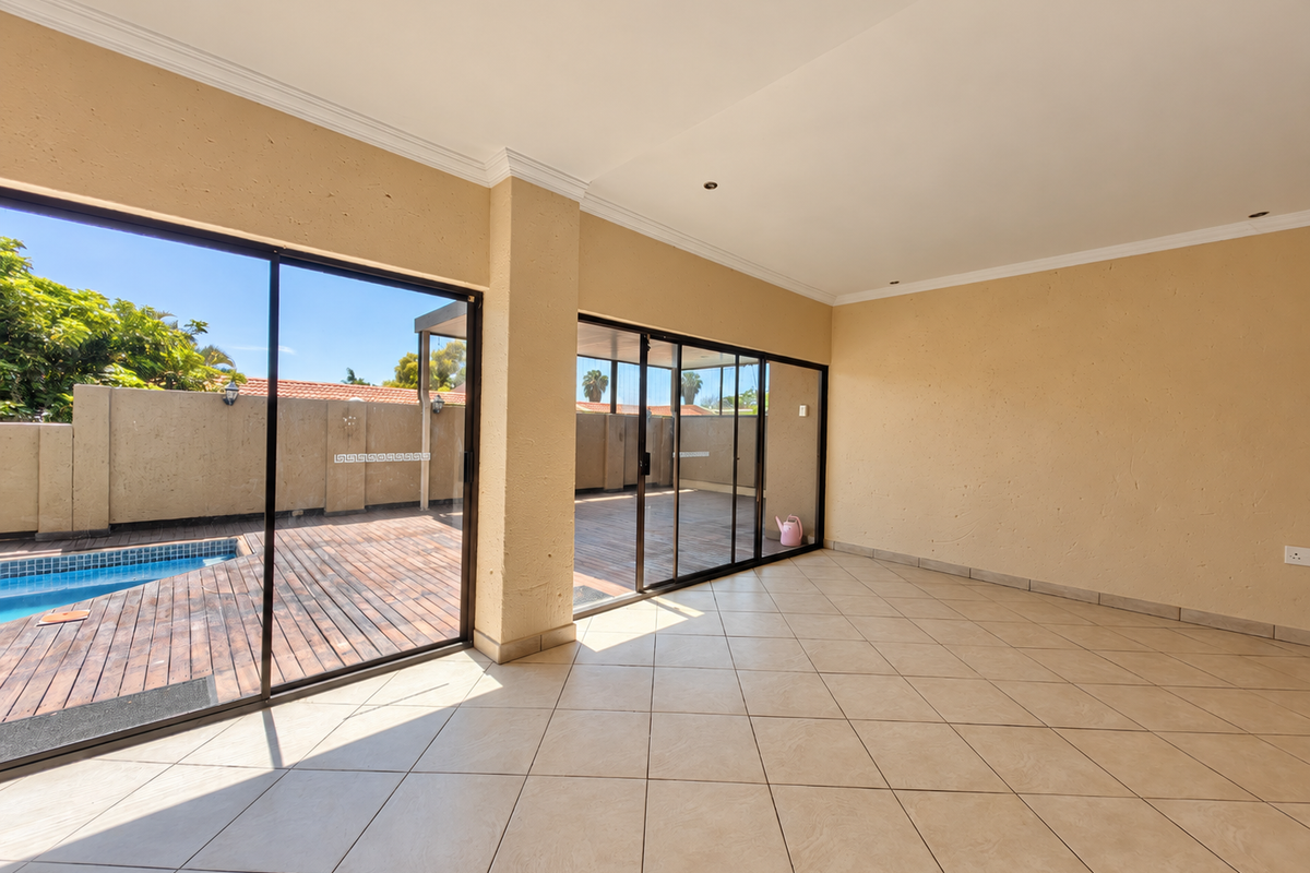 Spacious, empty living area featuring large sliding glass doors that open onto a wooden deck and swimming pool area.